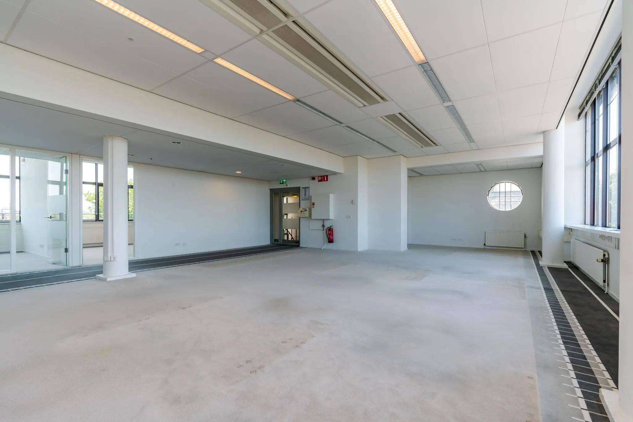 Leeg en licht kantoorruimte aan de Van Alkemadelaan met grote ramen en systeemplafond.